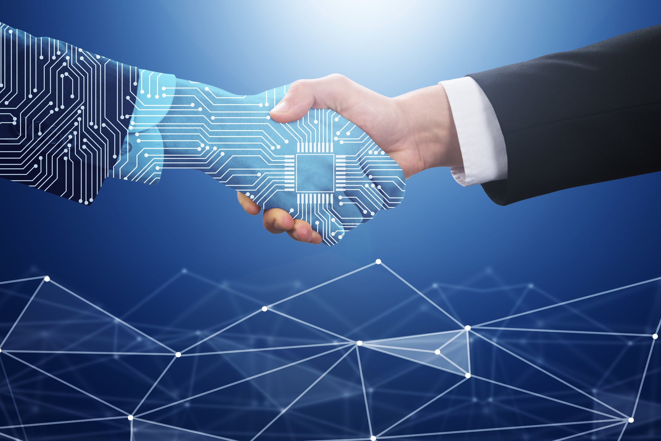 Conceptual depiction of collaboration between technology and a person, featuring a handshake between a human hand in a business suit and a hand overlaid with a blue circuit board pattern, which includes a central chip design.